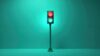 Traffic light shows red and green signals. Vertical pole supports signal box against teal backdrop. Minimalist design, simple shapes and colors.