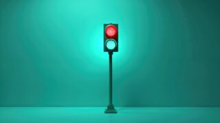 Traffic light shows red and green signals. Vertical pole supports signal box against teal backdrop. Minimalist design, simple shapes and colors.
